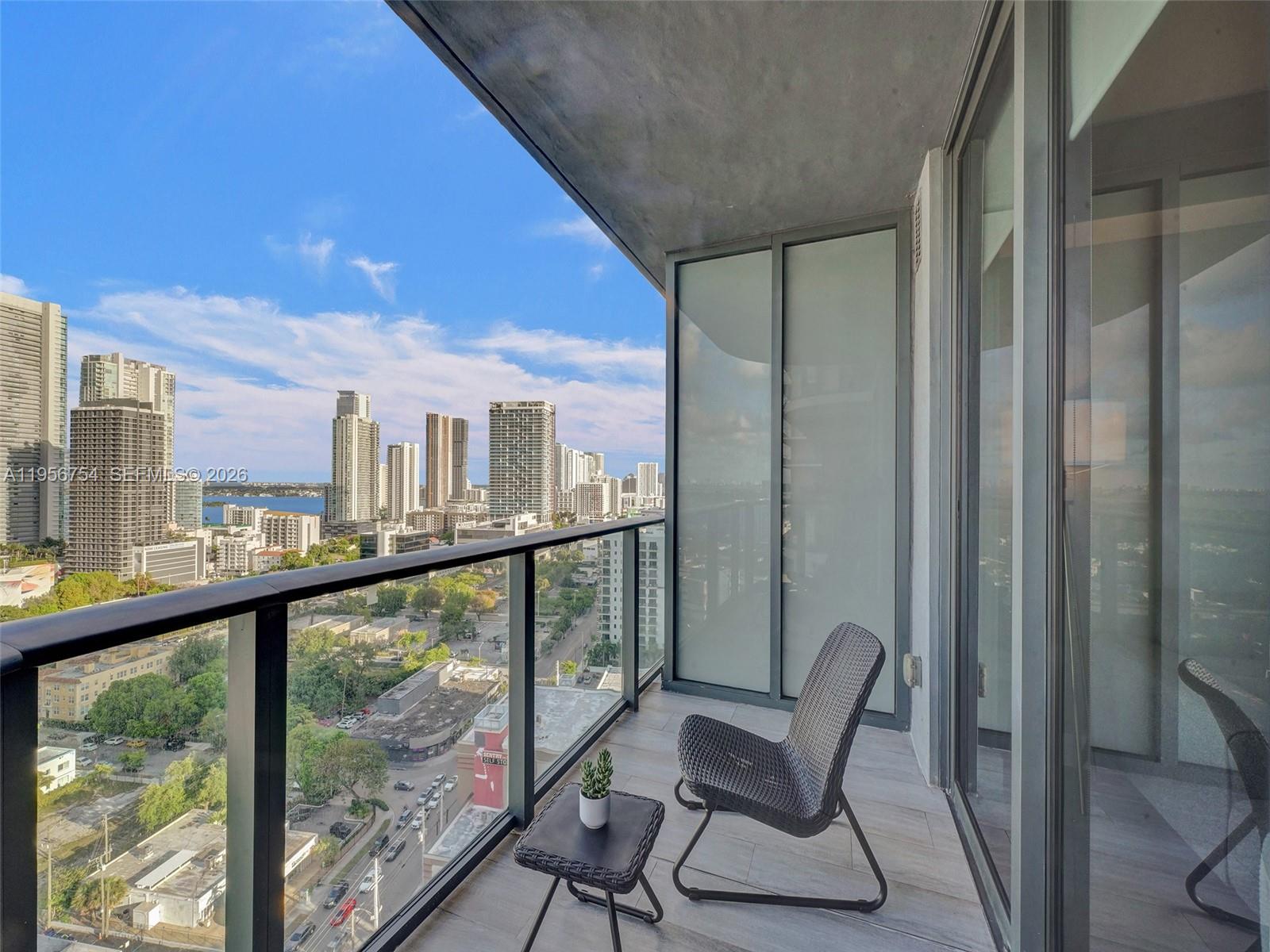A high-rise balcony features a modern chair, a small table, and a city skyline view — 121 NE 34th St # 2106A, Miami FL 33137, MIAMI, FL