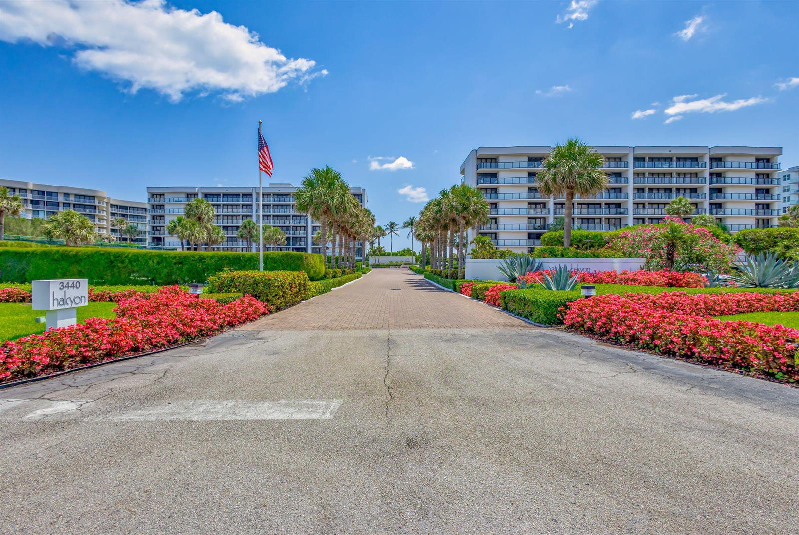 A paved driveway leads toward a multi-story apartment building lined with palm trees and flowers — 3440 S Ocean Boulevard # 204s, Palm Beach FL 33480, PALM BEACH, FL