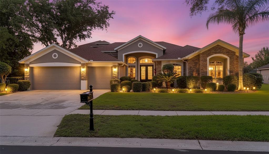 A single-story house with a three-car garage, stone accents, and a manicured lawn at dusk — 10354 OAKVIEW POINTE TERRACE, GOTHA, FL