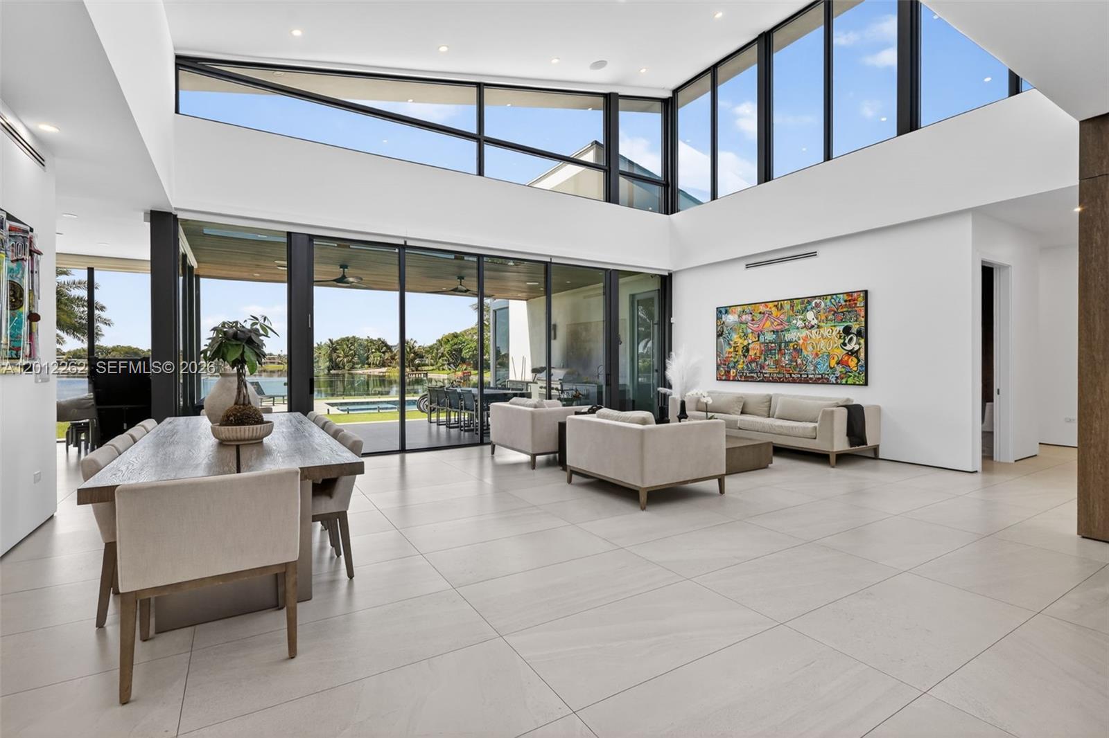 A modern open-concept living and dining area features floor-to-ceiling windows overlooking a pool and lake — 1830 NE 193rd St, Miami FL 33179, MIAMI, FL