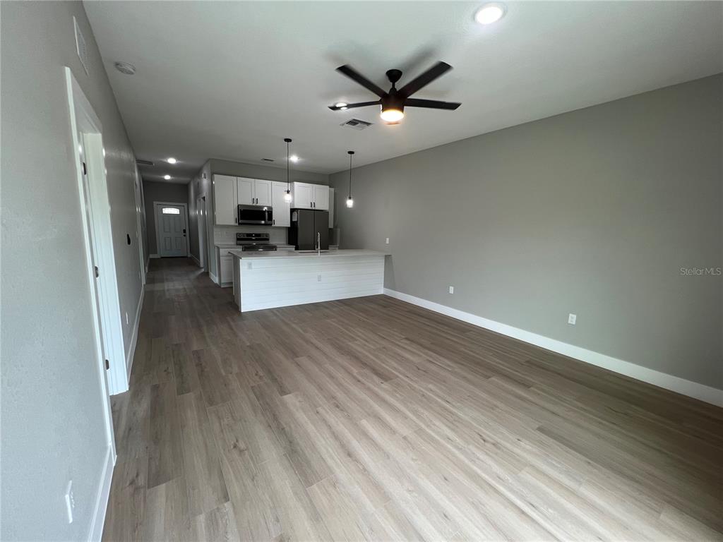 An open-concept kitchen and living area feature white cabinets, a breakfast bar, and wood-look flooring — 12130 HENLEY AVENUE, PORT CHARLOTTE, FL