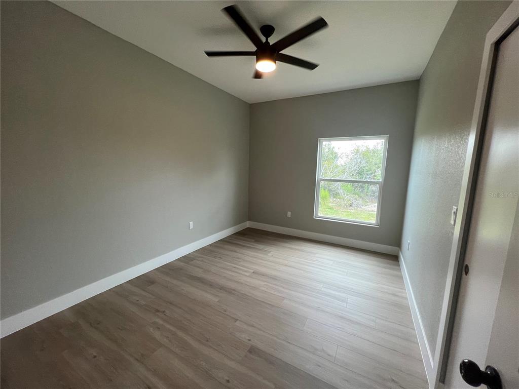 An empty bedroom features light gray walls, wood-look flooring, a ceiling fan, and a window — 12130 HENLEY AVENUE, PORT CHARLOTTE, FL
