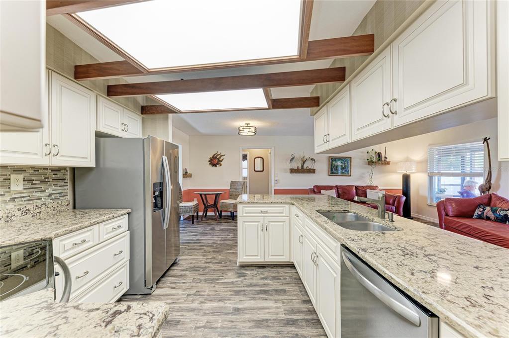 A kitchen with white cabinets, granite countertops, and wood ceiling beams opens to a living area — 1768 BANYAN DRIVE, VENICE, FL
