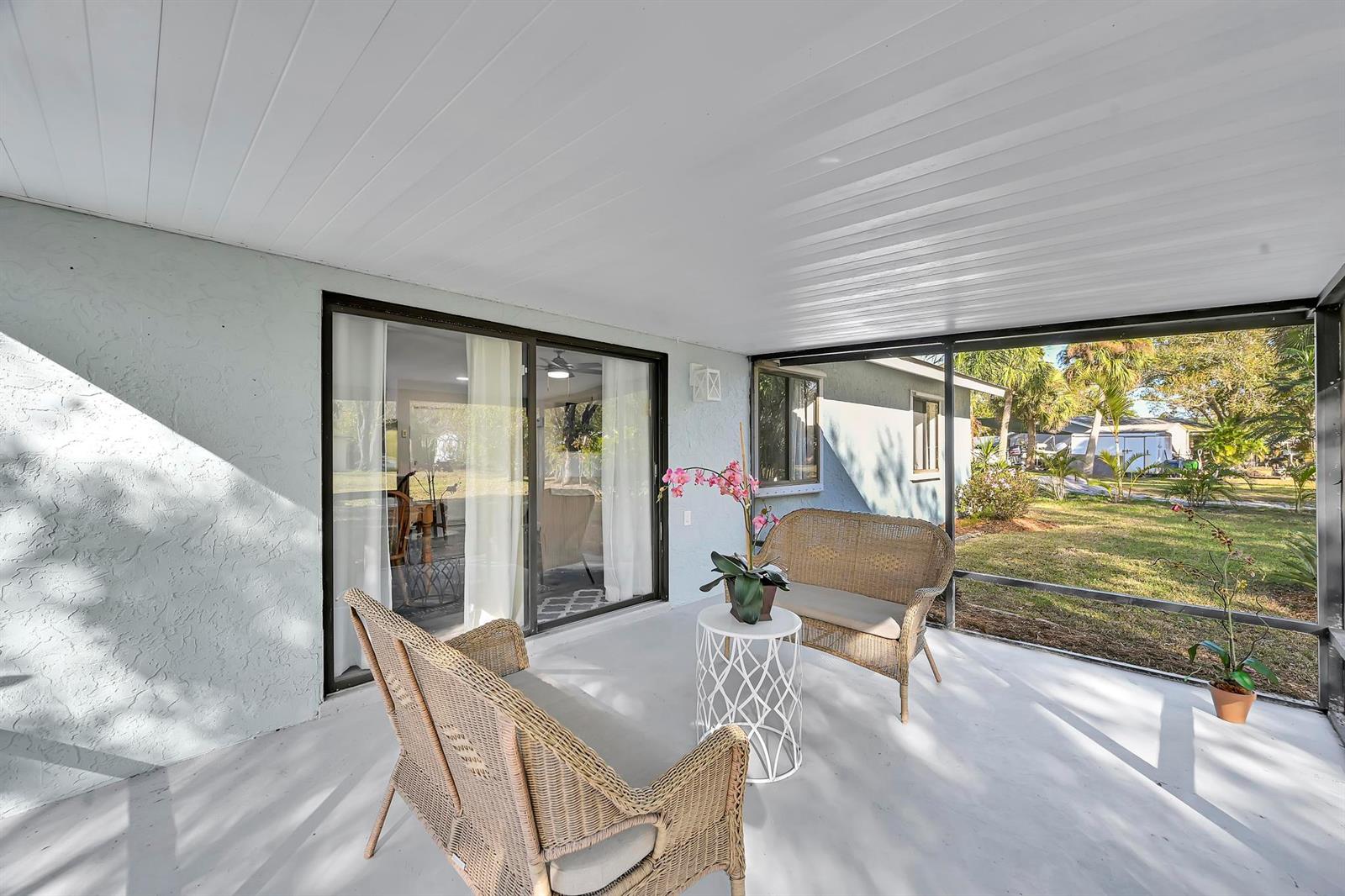 A screened-in patio features wicker furniture, a small white table, and sliding glass doors — 1765 24th Place SW, Vero Beach FL 32962, VERO BEACH, FL