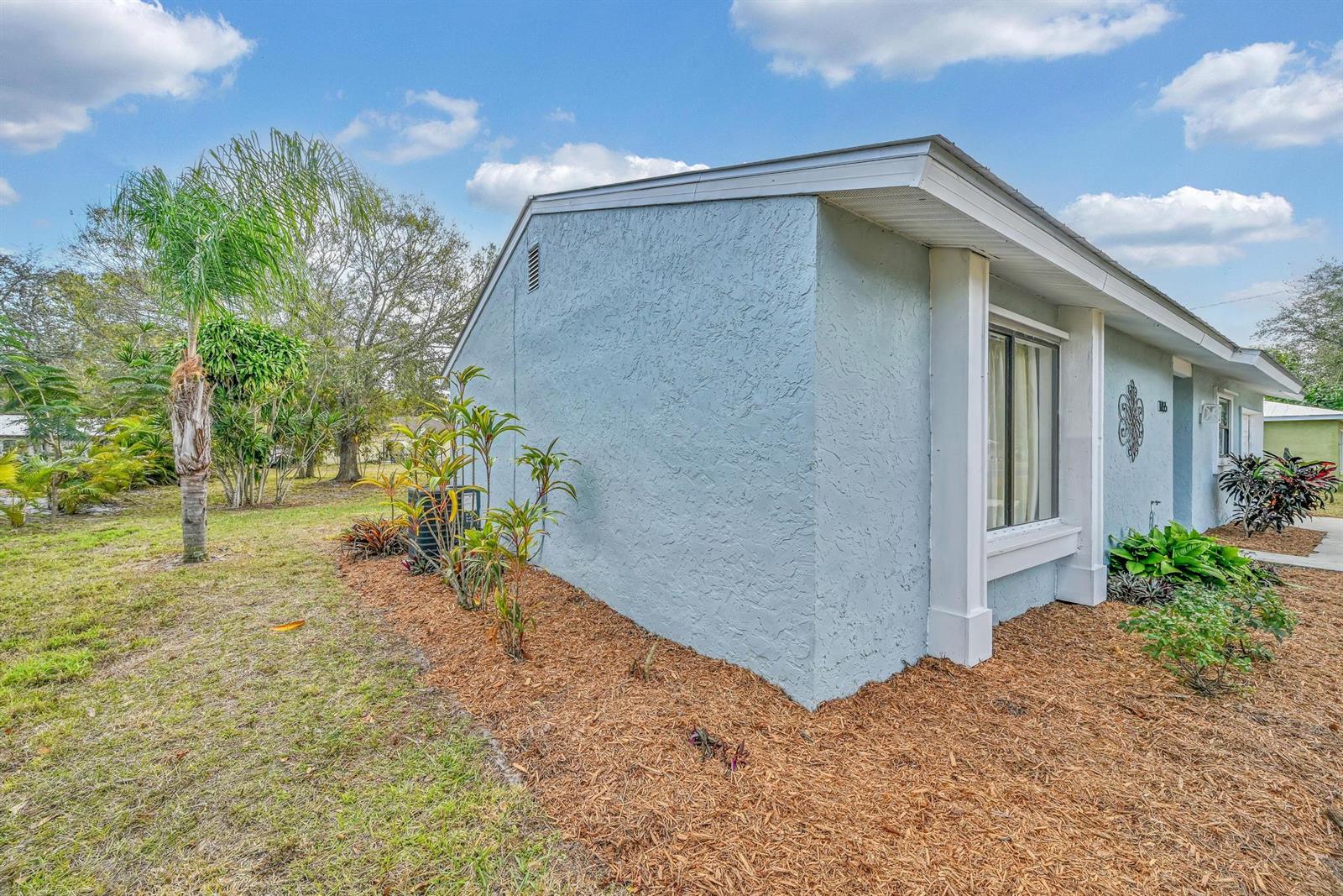 A light blue stucco house exterior features a side yard with mulch and palm trees — 1765 24th Place SW, Vero Beach FL 32962, VERO BEACH, FL