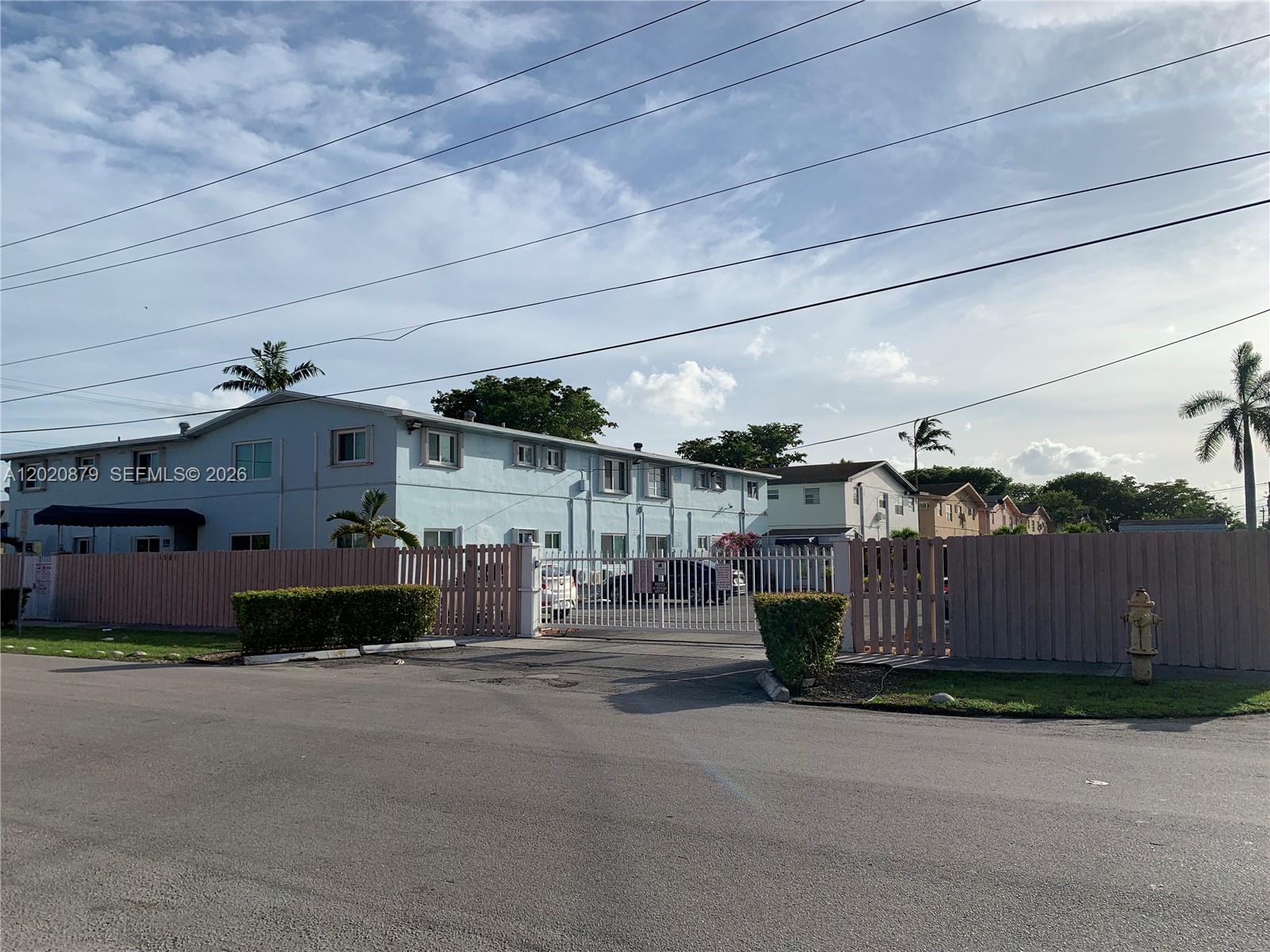A light blue two-story apartment building is enclosed by a tan fence and gated entrance — 1581 NE 8th St # 7, Homestead FL 33033, HOMESTEAD, FL