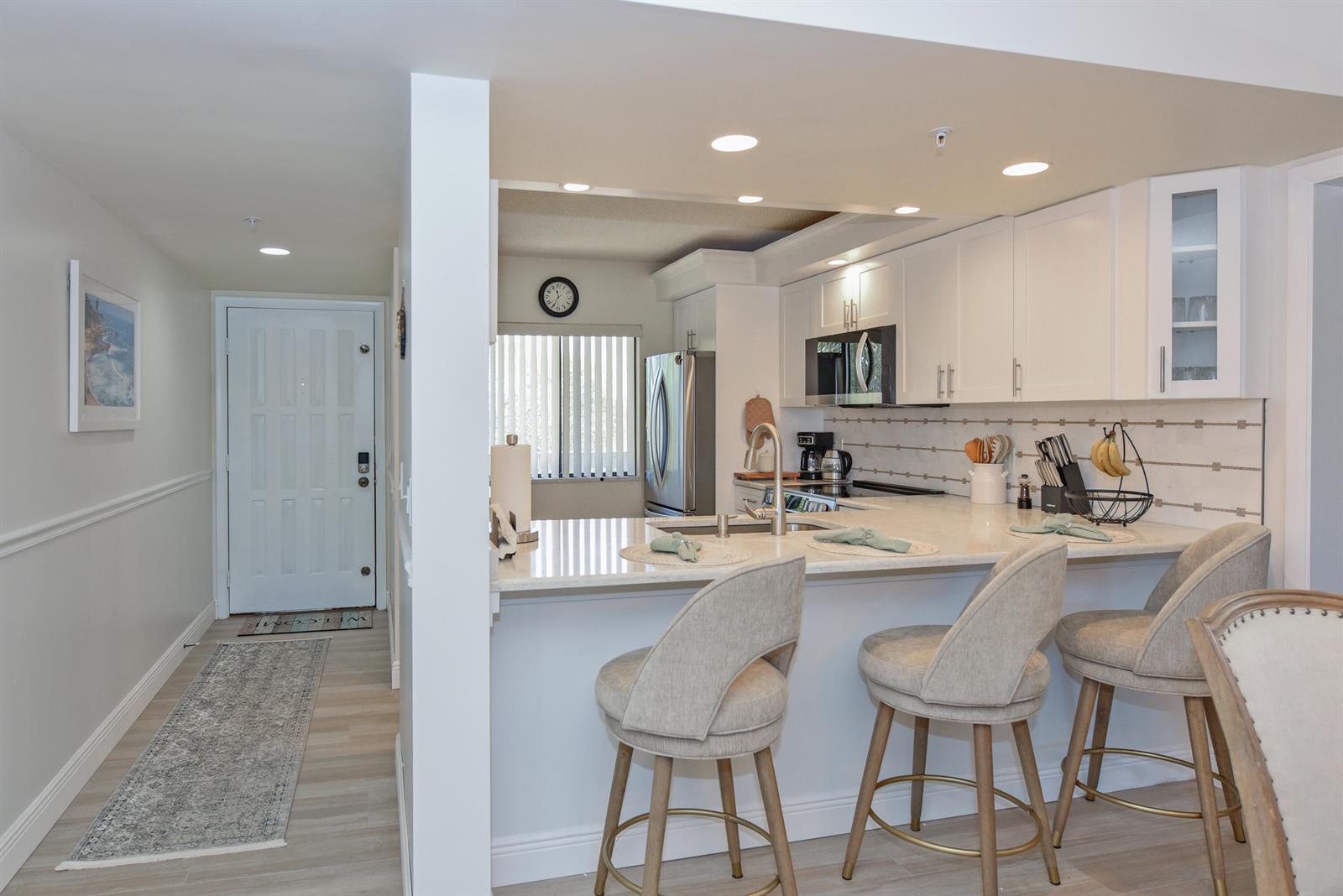 A kitchen with white cabinets, stone countertops, and a breakfast bar with three stools — 901 Seafarer Circle # 302, Jupiter FL 33477, JUPITER, FL