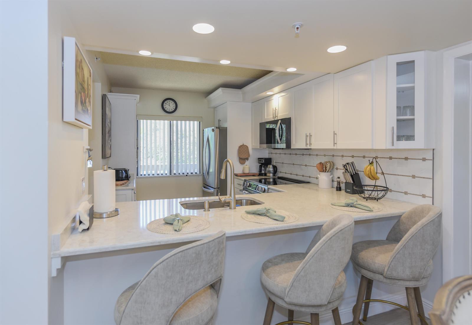 A kitchen with white cabinets, light countertops, a breakfast bar, and three upholstered stools — 901 Seafarer Circle # 302, Jupiter FL 33477, JUPITER, FL
