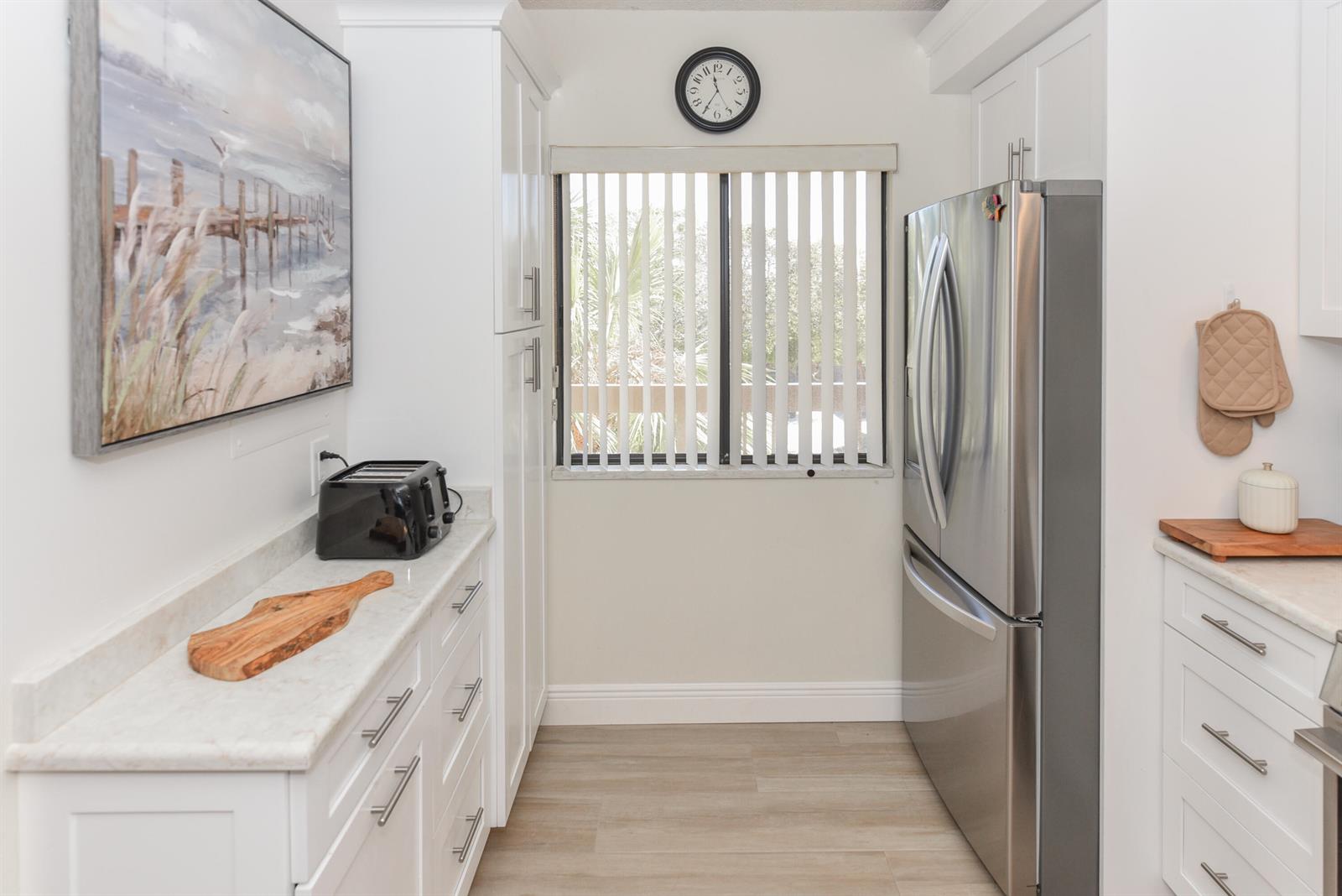 A bright kitchen features white cabinets, marble countertops, stainless steel appliances, and a window with blinds — 901 Seafarer Circle # 302, Jupiter FL 33477, JUPITER, FL