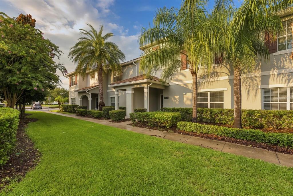 A two-story townhouse exterior with palm trees, a green lawn, and a concrete walkway — 4879 CLOCK TOWER DRIVE, KISSIMMEE, FL