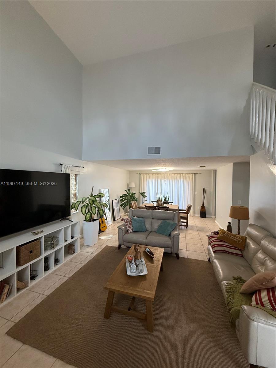 A living room with high ceilings, tile flooring, a large television, and a dining area — 18164 SW 149th Pl, Miami FL 33187, MIAMI, FL