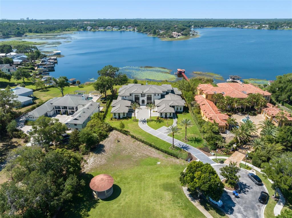 An aerial view shows a large modern house with a circular driveway near a lake — 3057 PORTO LAGO COURT, WINDERMERE, FL