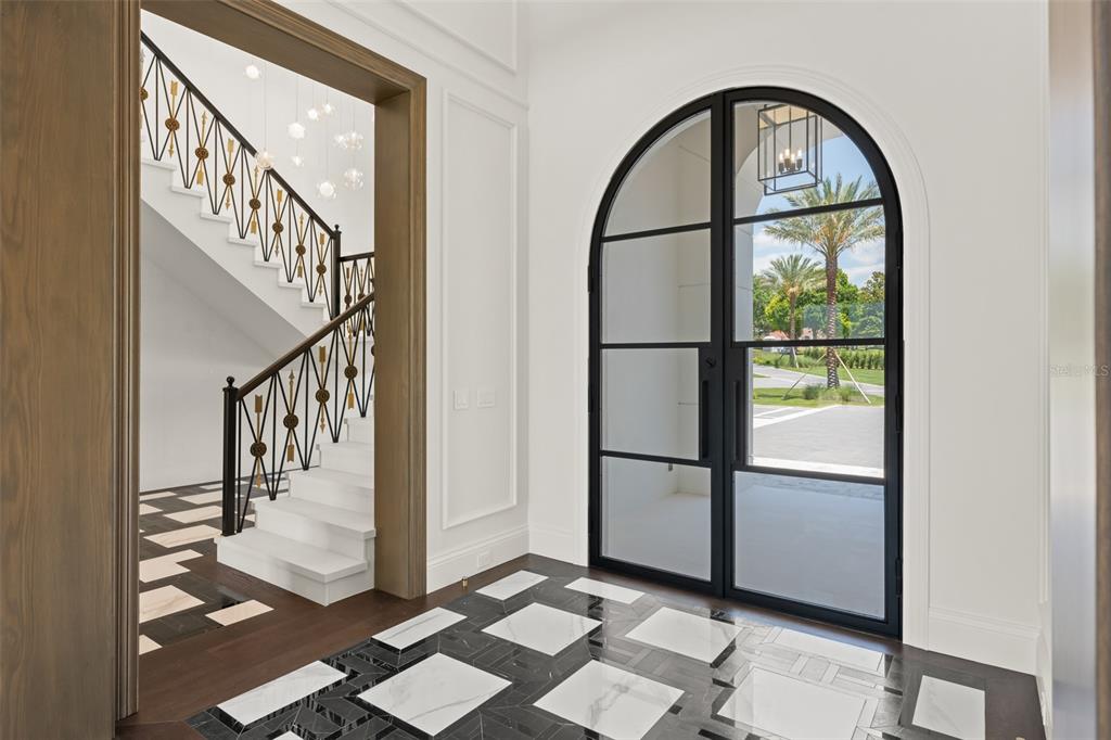 An entryway features a black arched glass door, marble tile flooring, and a staircase nearby — 3057 PORTO LAGO COURT, WINDERMERE, FL