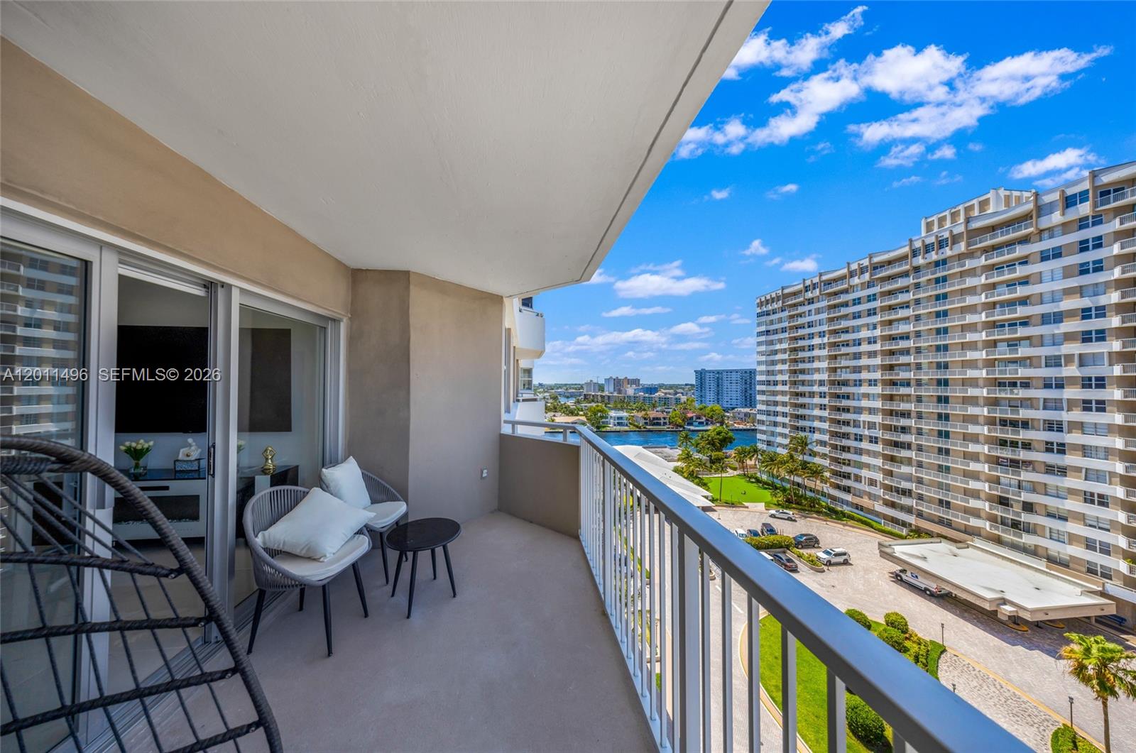 A balcony with two chairs and a small table overlooks a parking lot and waterway — 1985 S Ocean Dr # 10B, Hallandale Beach FL 33009, HALLANDALE BEACH, FL