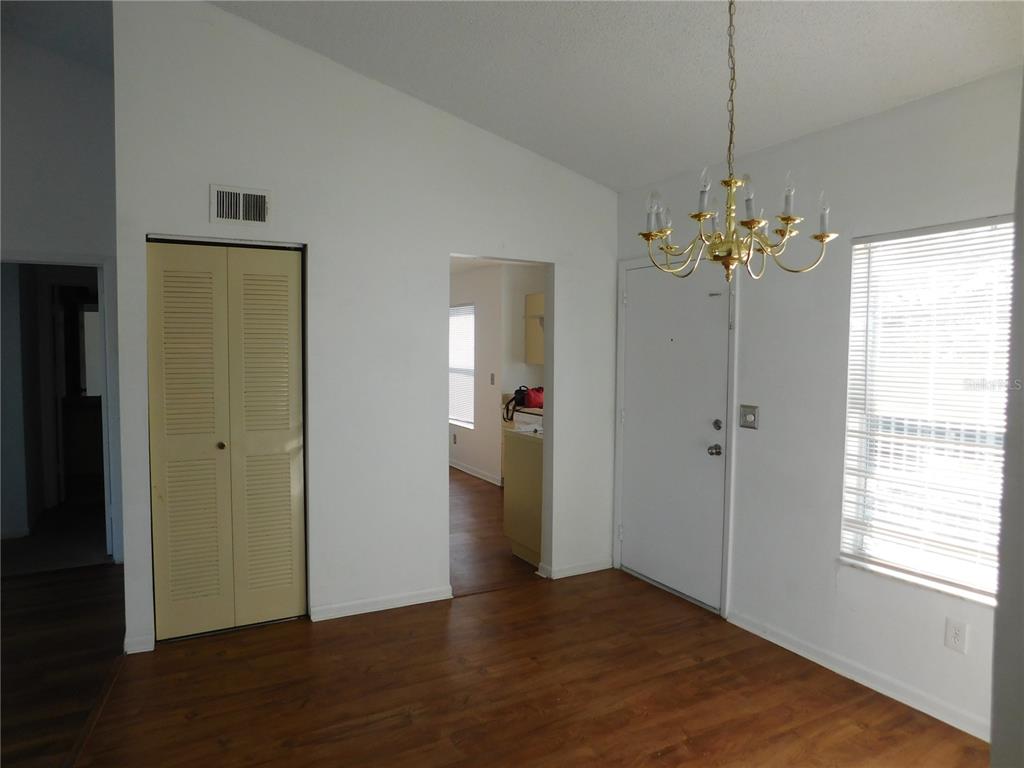A dining area features wood-look flooring, a brass chandelier, a white door, and louvered closet doors — 2540 WOODGATE BOULEVARD UNIT 204, ORLANDO, FL