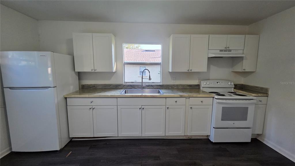 A kitchen features white cabinets, white appliances, a stainless steel sink, and dark wood flooring — 1135 FAIRVIEW AVENUE, BARTOW, FL