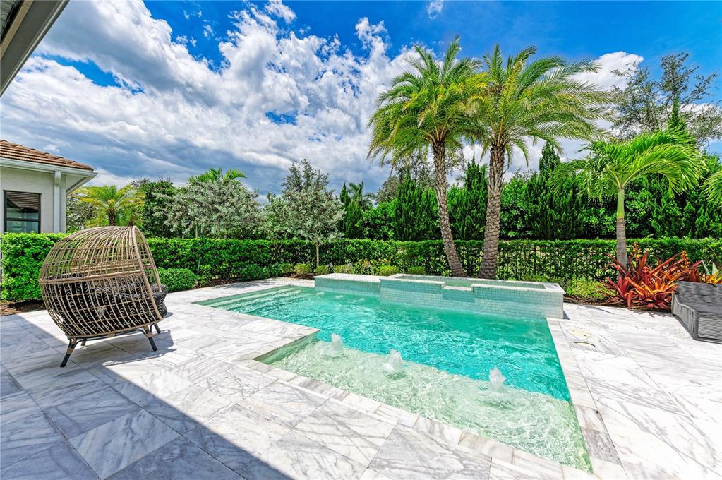 A backyard features a rectangular swimming pool with fountains, palm trees, and marble patio tiles — 5060 SIMONS COURT, LAKEWOOD RANCH, FL