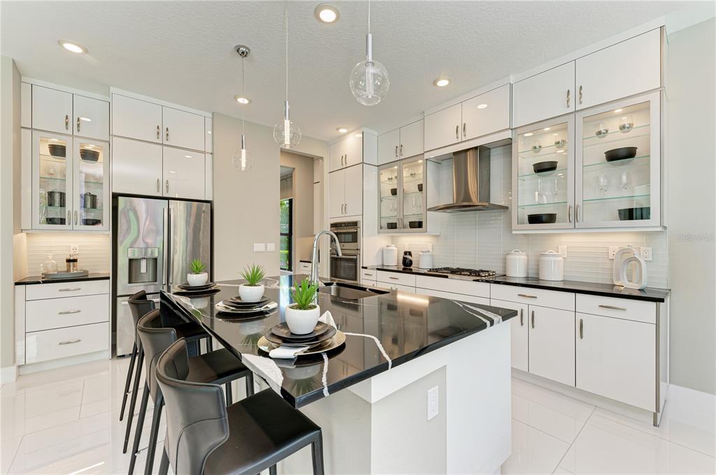 A modern kitchen features white cabinetry, a black granite island, and stainless steel appliances — 5060 SIMONS COURT, LAKEWOOD RANCH, FL