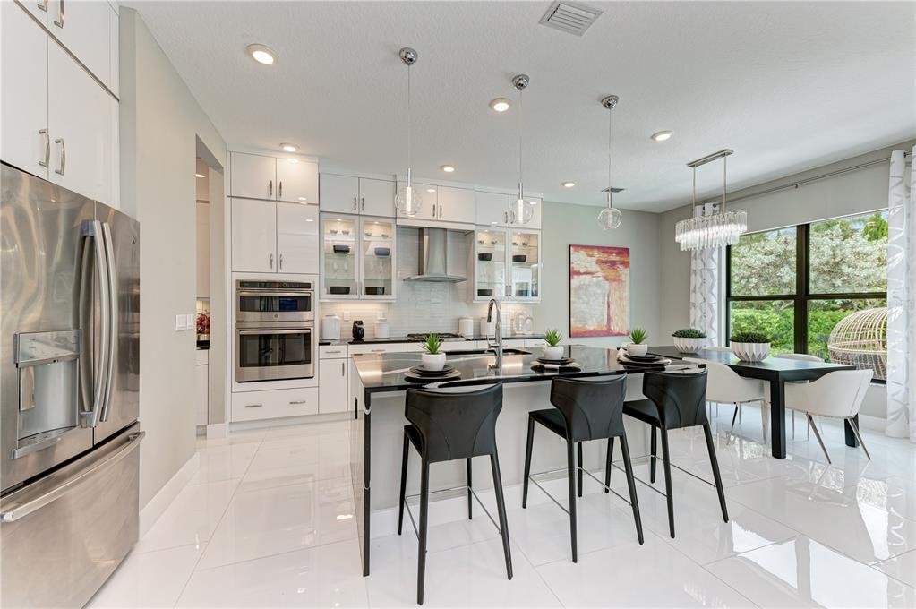 A modern kitchen features white cabinetry, a black island with bar stools, and tile flooring — 5060 SIMONS COURT, LAKEWOOD RANCH, FL