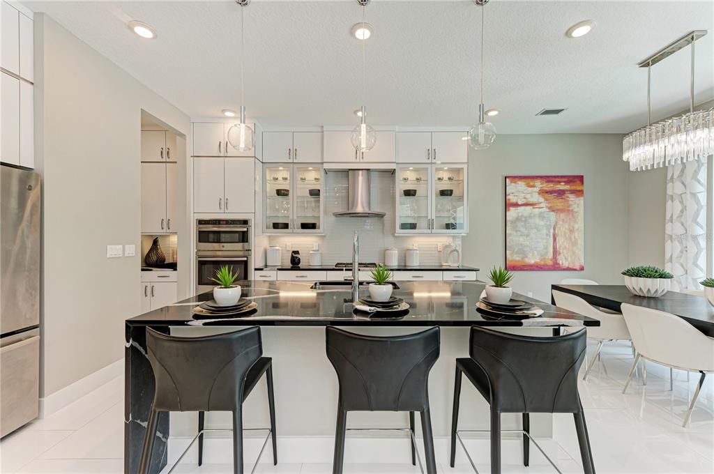 A modern kitchen features a black marble island, white cabinetry, and three black bar stools — 5060 SIMONS COURT, LAKEWOOD RANCH, FL