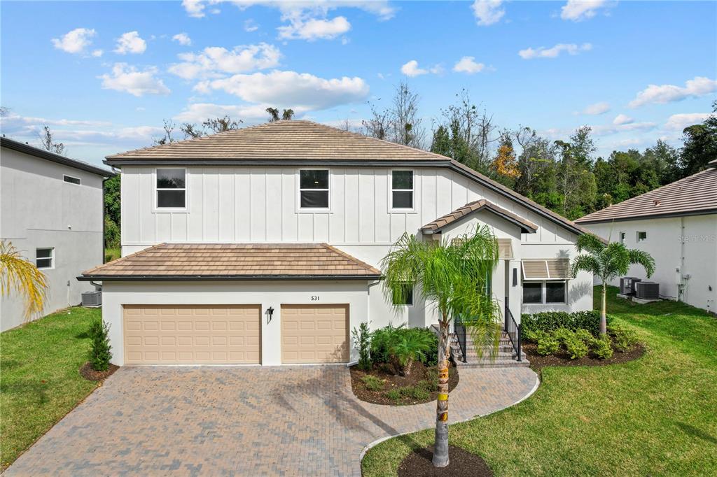 A two-story house with a white board-and-batten facade, tan tile roof, and two-car garage — 531 SANCTUARY GOLF PLACE, APOPKA, FL