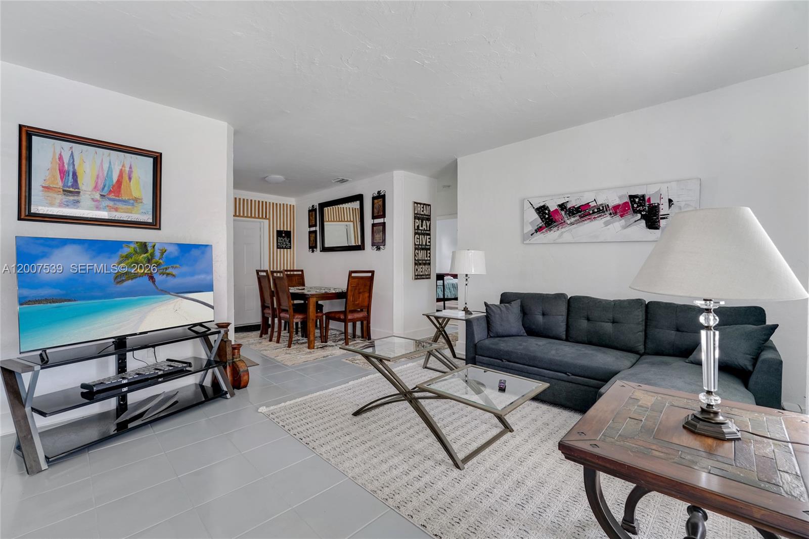 A living room with a grey sectional, glass coffee tables, and an adjacent dining area — 1283 NW 45th St, Miami FL 33142, MIAMI, FL