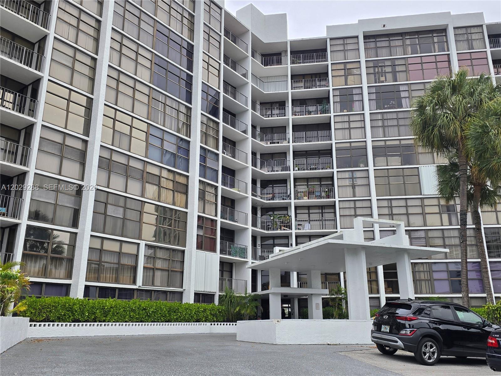 A multi-story residential building with balconies and a covered entrance stands beside a parked car — 400 Leslie Dr # 416, Hallandale Beach FL 33009, HALLANDALE BEACH, FL
