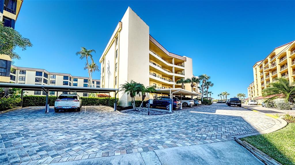 A paved parking area sits beneath a covered structure in front of multi-story apartment buildings — 8764 MIDNIGHT PASS ROAD UNIT A306, SARASOTA, FL