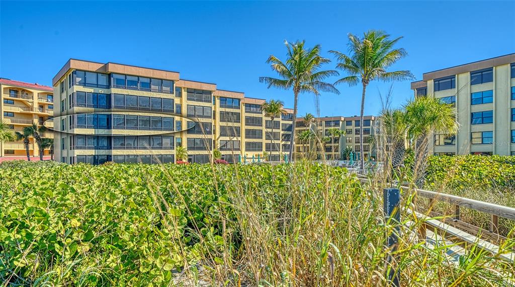 A sunroom features wood-look tile flooring, a wicker chair, and a large windowed wall — 8764 MIDNIGHT PASS ROAD UNIT A306, SARASOTA, FL