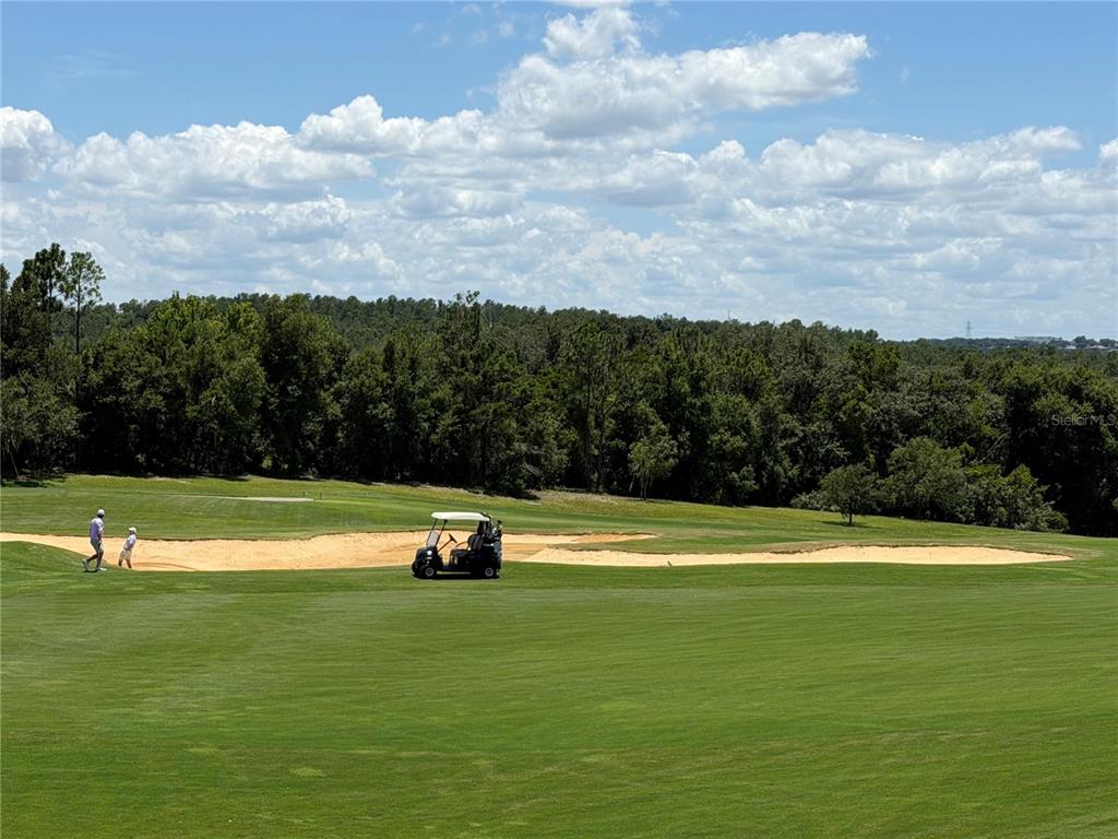 A golf course features a sand bunker, a golf cart, and two people walking nearby — 16038 VETTA DRIVE, BELLA COLLINA, FL