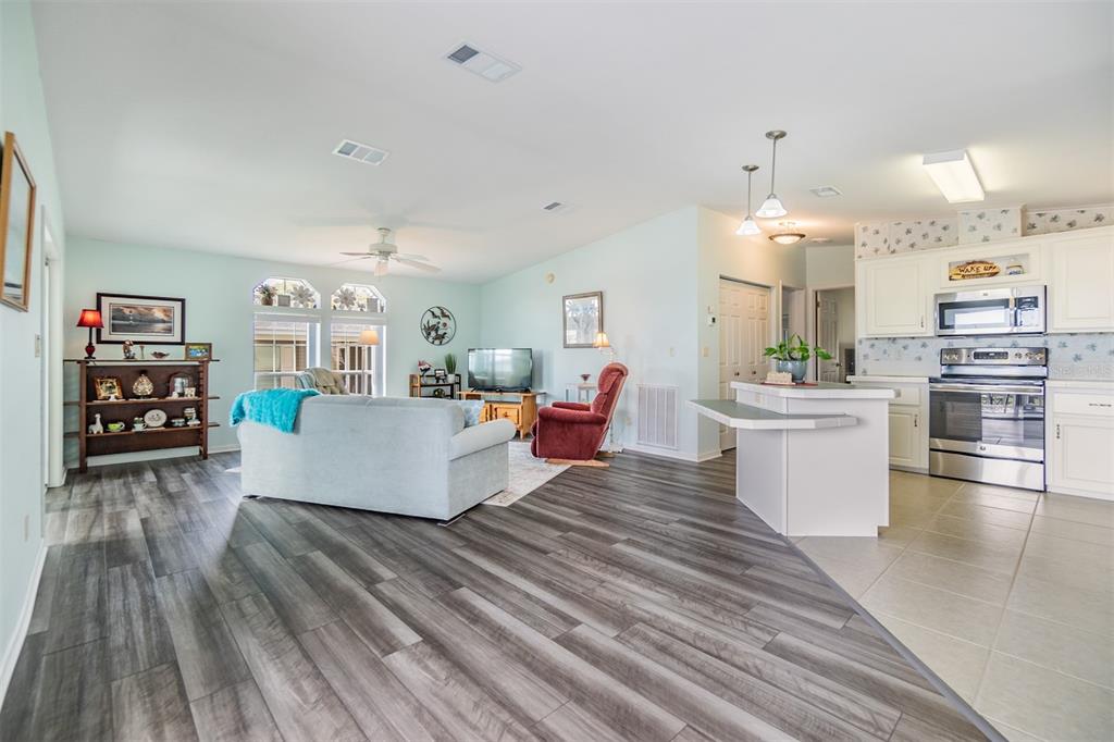 An open-concept living room and kitchen featuring wood-look flooring, white cabinetry, and stainless appliances — 37443 GILL AVENUE, ZEPHYRHILLS, FL