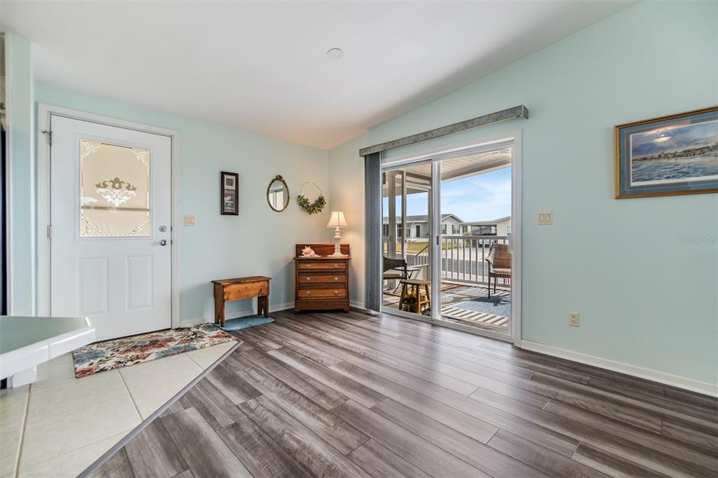 A living area with light blue walls, wood-look flooring, a white door, and sliding glass doors — 37443 GILL AVENUE, ZEPHYRHILLS, FL