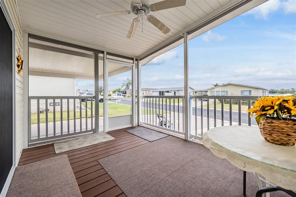 A screened-in porch features a ceiling fan, brown decking, and a view of neighboring homes — 37443 GILL AVENUE, ZEPHYRHILLS, FL