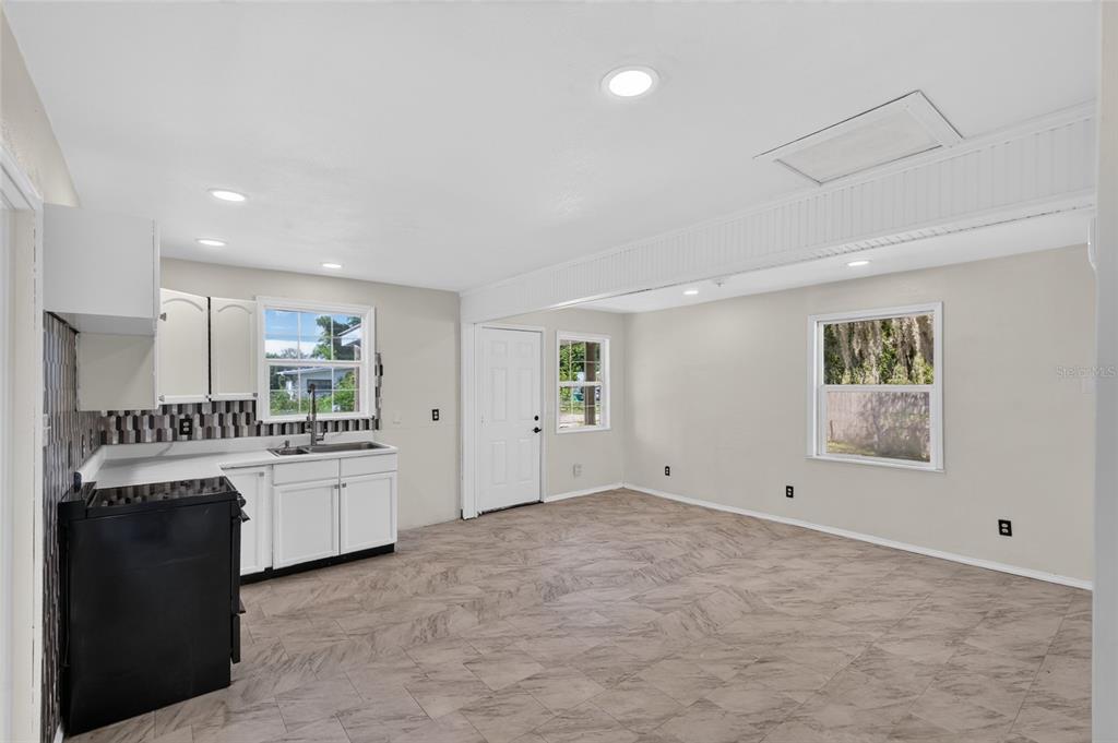 A kitchen and living area with white cabinets, a black stove, and light-colored tile flooring — 8024 HILLMAN AVENUE, PUNTA GORDA, FL