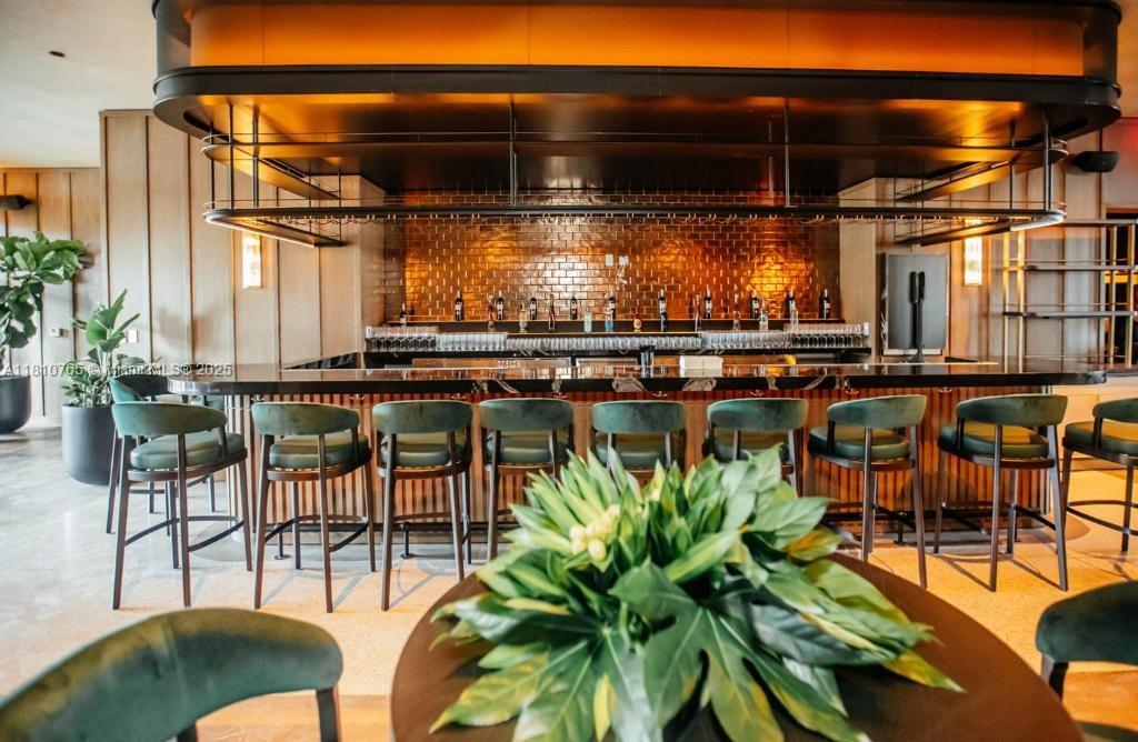 A modern bar area features green upholstered stools, a dark countertop, and a metallic backsplash — 159 NE 6TH ST # 3205, Miami FL 33132, MIAMI, FL