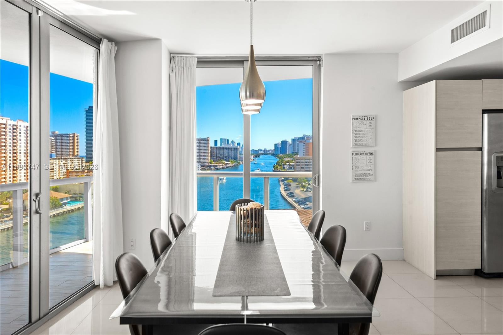 A dining room features a long table with eight chairs and floor-to-ceiling windows overlooking a waterway — 2600 E Hallandale Beach Blvd # T1001, Hallandale Beach FL 33009, HALLANDALE BEACH, FL