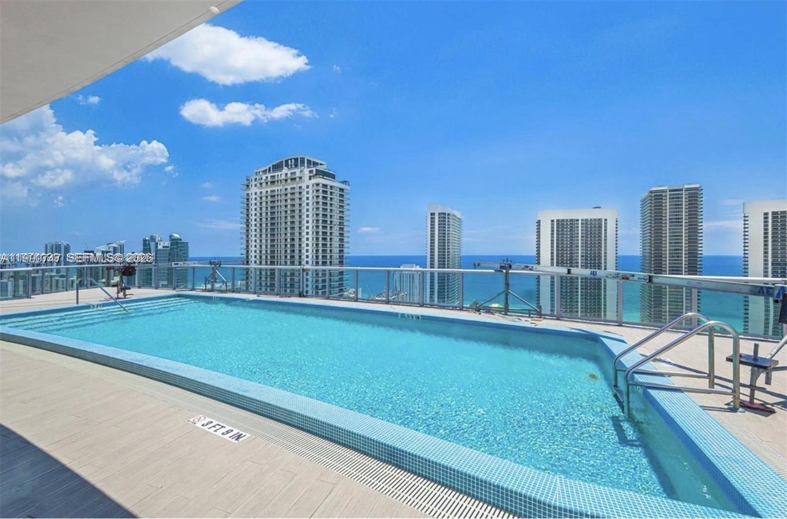 An outdoor swimming pool with a glass railing overlooks the ocean and city skyline — 2600 E Hallandale Beach Blvd # T1001, Hallandale Beach FL 33009, HALLANDALE BEACH, FL