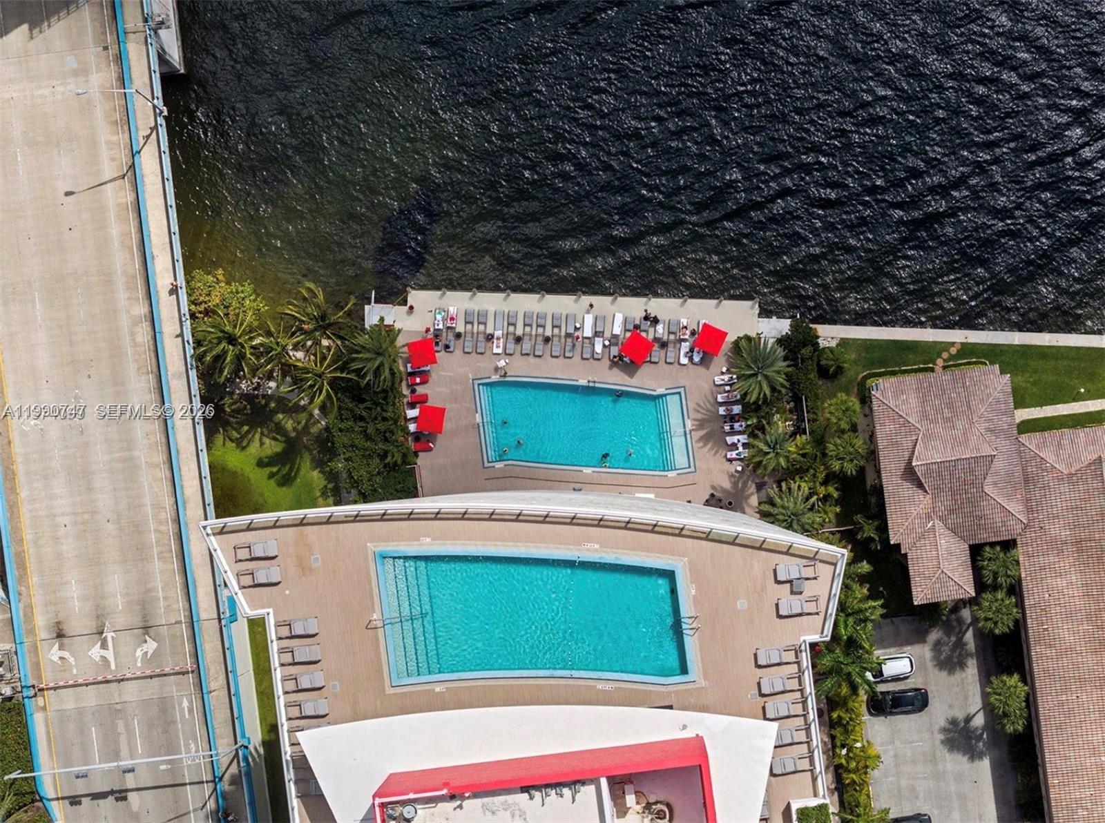 An aerial view shows two swimming pools, lounge chairs, and a bridge next to water — 2600 E Hallandale Beach Blvd # T1001, Hallandale Beach FL 33009, HALLANDALE BEACH, FL