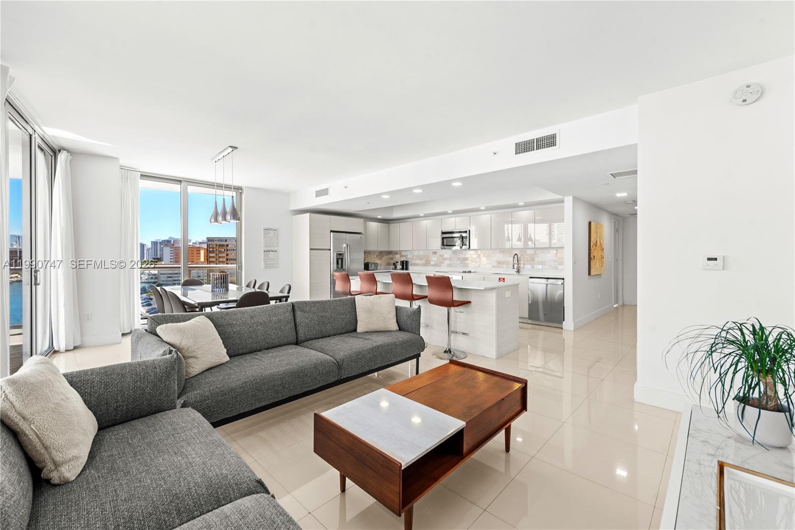 A modern open-concept living room and kitchen with gray furniture, tile floors, and city views — 2600 E Hallandale Beach Blvd # T1001, Hallandale Beach FL 33009, HALLANDALE BEACH, FL