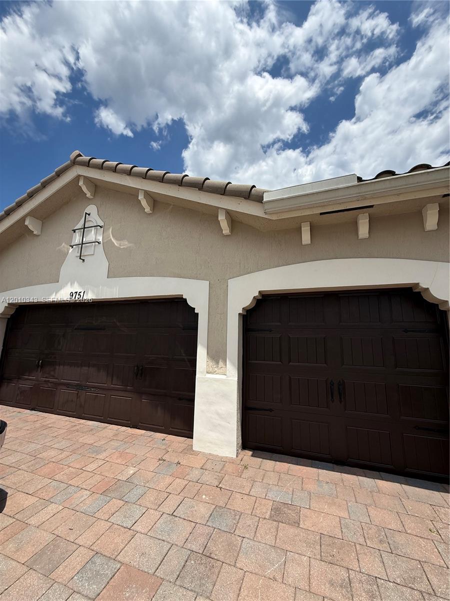 A beige house exterior features two dark brown garage doors and a paved driveway — 9751 Lakeview Ln, Parkland FL 33076, PARKLAND, FL