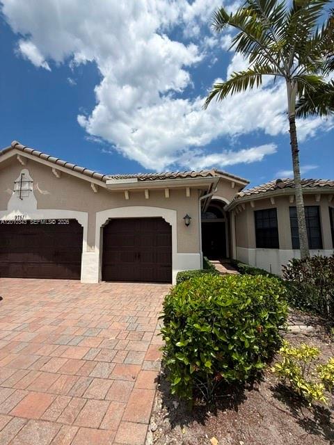 A beige house features a paved driveway, dark garage doors, and a tall palm tree — 9751 Lakeview Ln, Parkland FL 33076, PARKLAND, FL