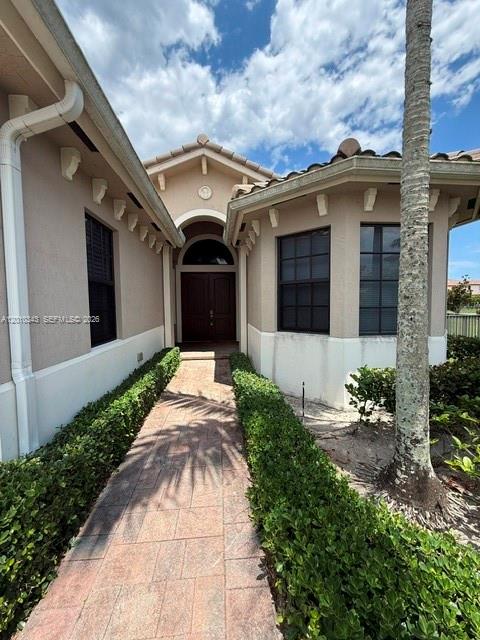 A paved walkway leads to the front entrance of a beige house with dark windows — 9751 Lakeview Ln, Parkland FL 33076, PARKLAND, FL