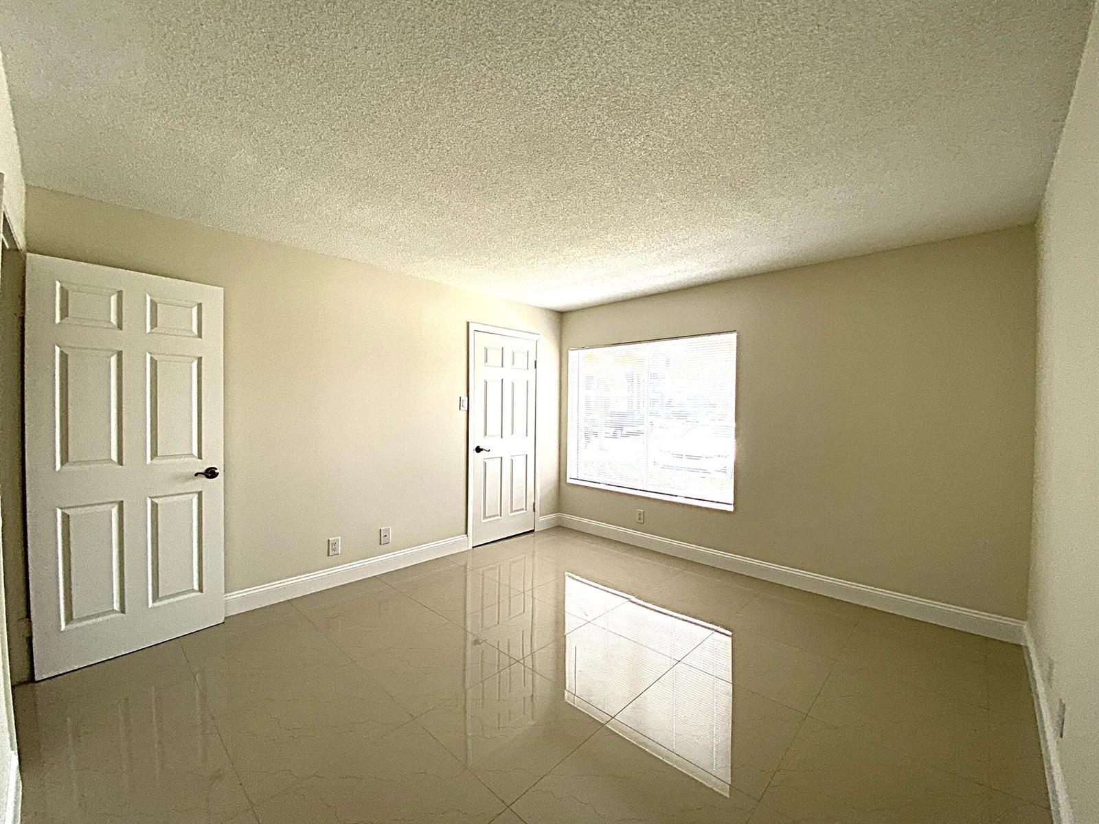 An empty room features beige walls, a popcorn ceiling, and glossy light-colored tile flooring — 815 W Boynton Beach Boulevard # 102, Boynton Beach FL 33426, BOYNTON BEACH, FL