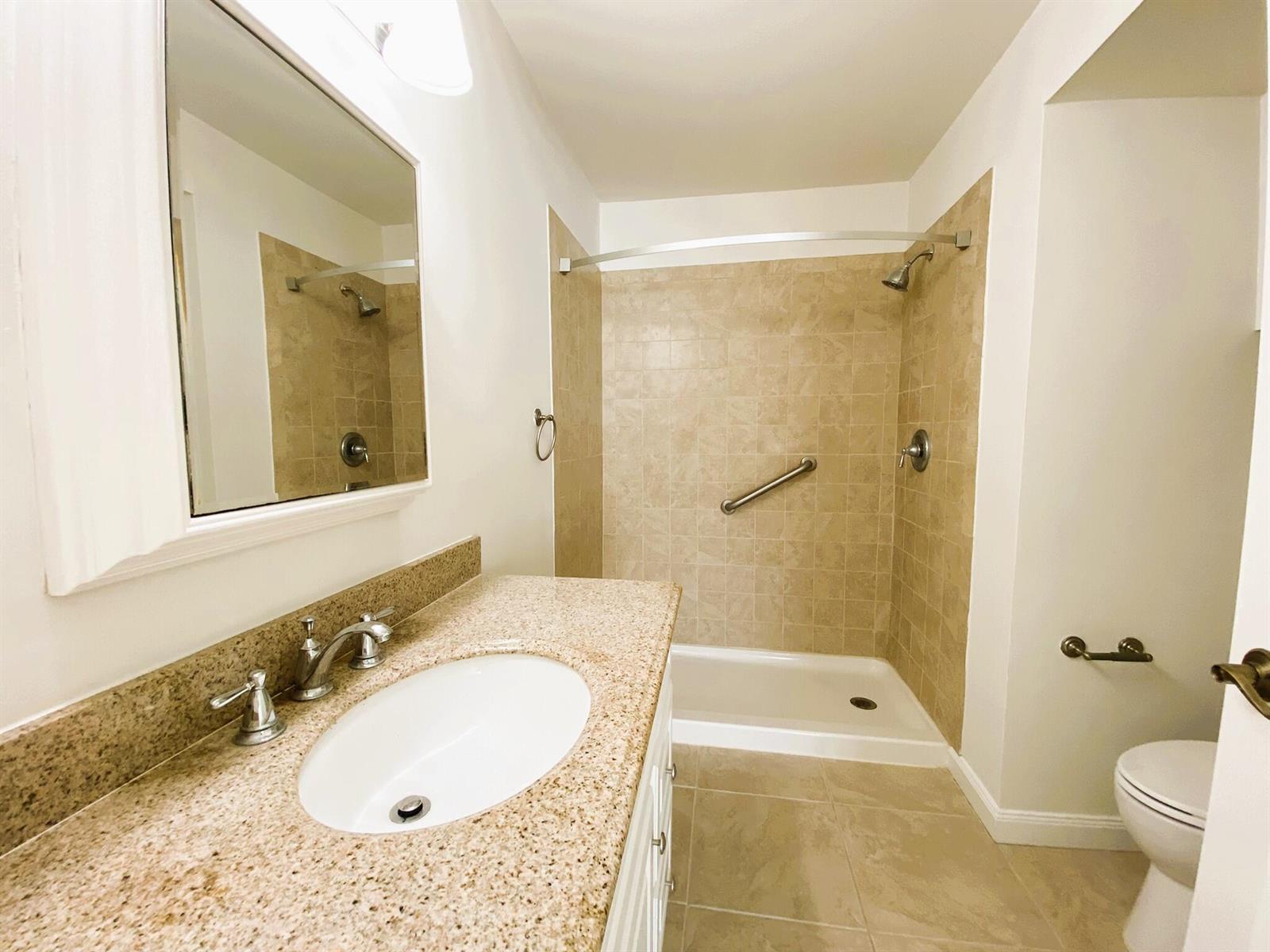 A bathroom featuring a granite vanity, a walk-in shower with beige tiles, and a toilet — 815 W Boynton Beach Boulevard # 102, Boynton Beach FL 33426, BOYNTON BEACH, FL