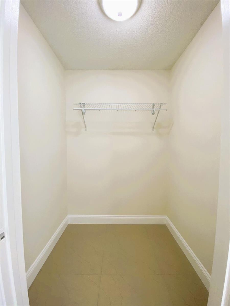 A small walk-in closet with beige tile flooring, white walls, and a single wire shelf — 815 W Boynton Beach Boulevard # 102, Boynton Beach FL 33426, BOYNTON BEACH, FL