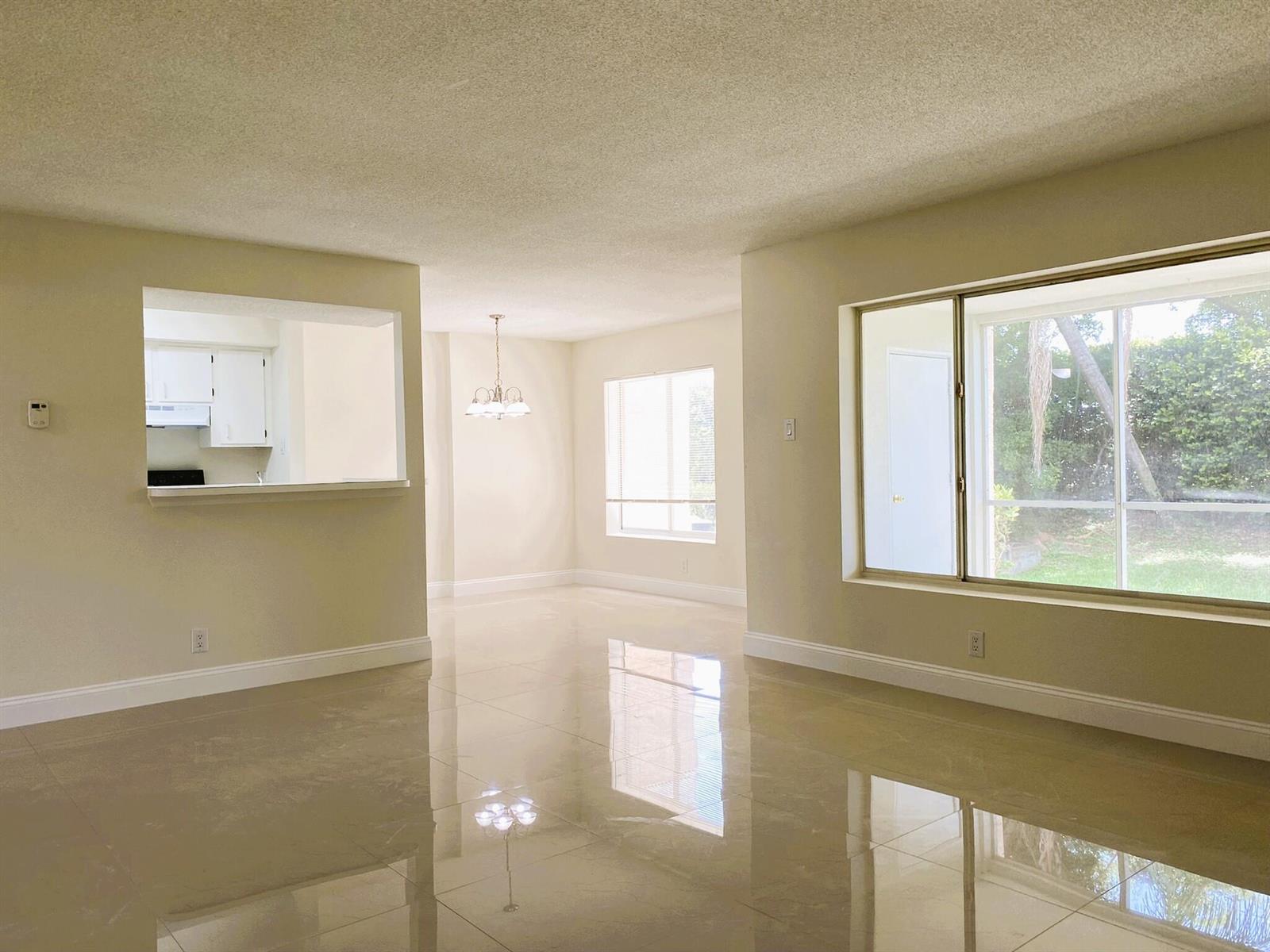 An empty living room with glossy tile floors, a kitchen pass-through, and large windows — 815 W Boynton Beach Boulevard # 102, Boynton Beach FL 33426, BOYNTON BEACH, FL