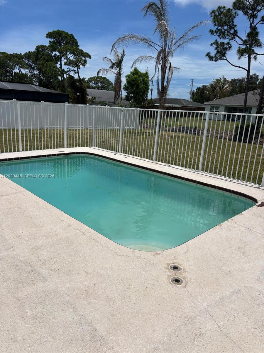 A rectangular swimming pool sits on a concrete patio enclosed by a white fence — PORT ST. LUCIE, FL