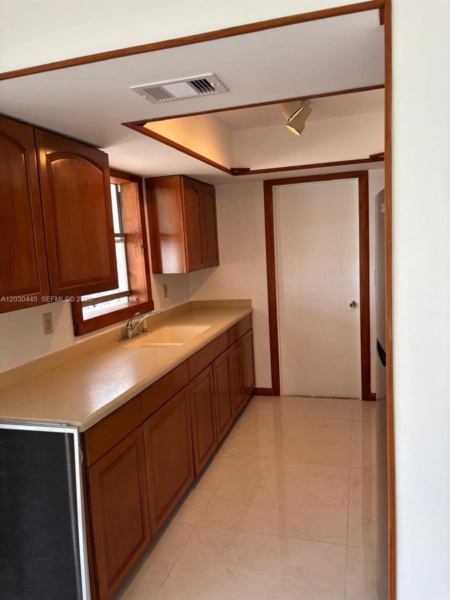A galley-style kitchen features wood cabinets, light countertops, and tile flooring — PORT ST. LUCIE, FL