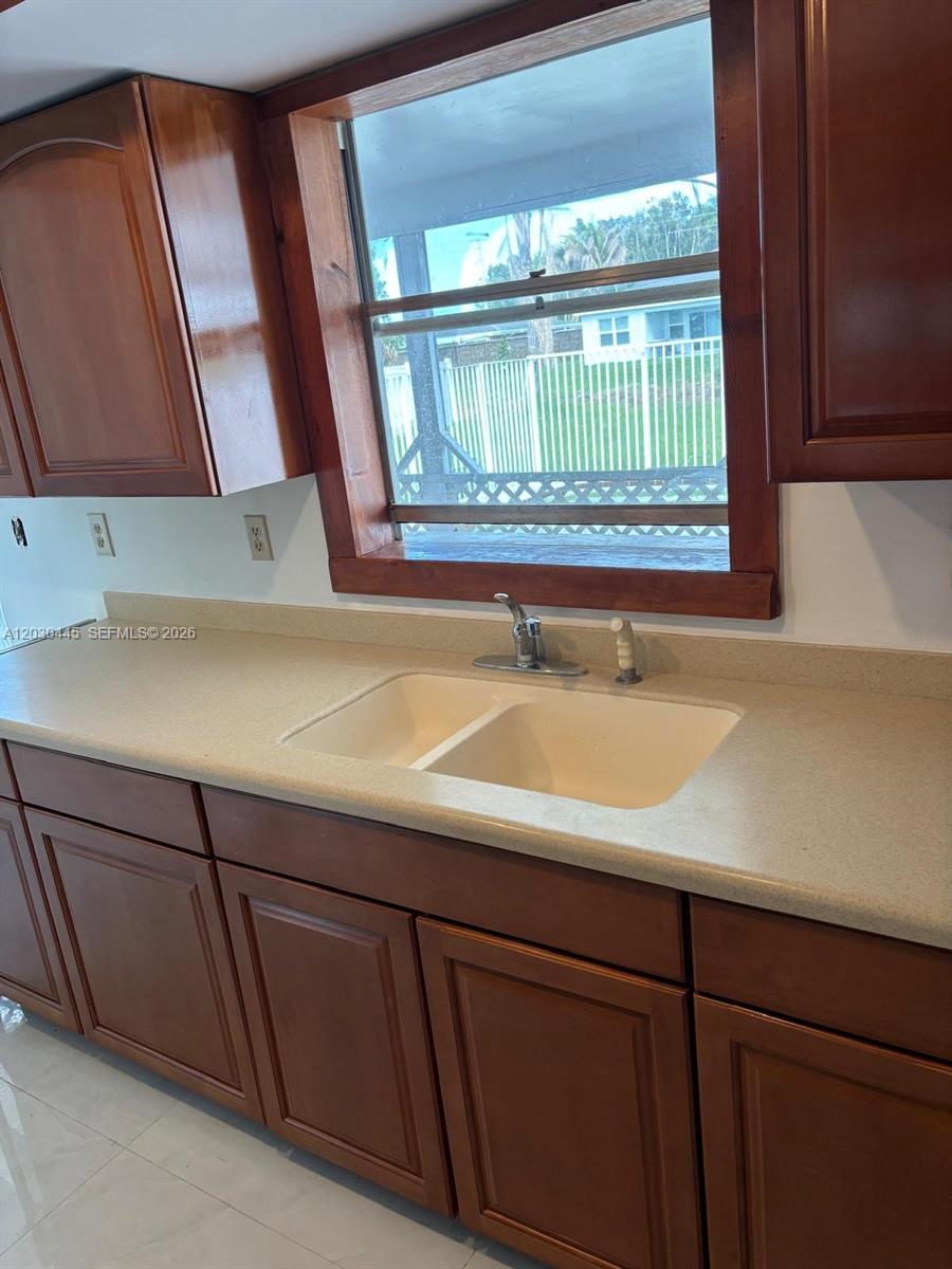 A kitchen features wooden cabinets, a double-basin sink, and a window overlooking a backyard — PORT ST. LUCIE, FL