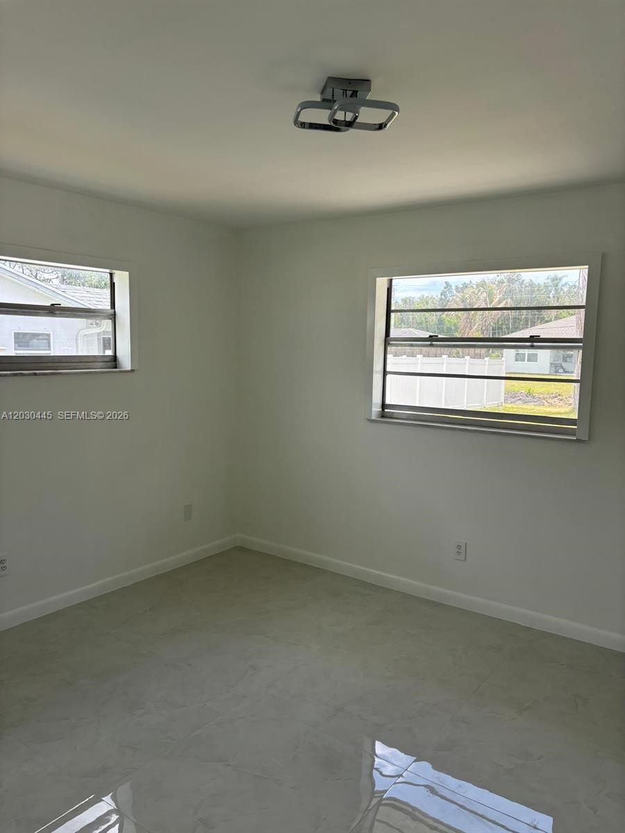 A bright, empty bedroom features white walls, light-colored tile flooring, and two windows — PORT ST. LUCIE, FL